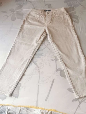 Beiga raka jeans från Gina Tricot - Snygga beiga jeans från Gina Tricot med rak passform och klassisk femficksdesign. Jeansen har normal midja och stängs med knapp och dragkedja. Perfekta för en clean och stilren look. Materialet är denim i bomull.