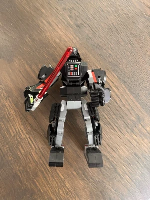Lego Darth Vader robotfigur - Säljer en svart och grå Darth Vader robotfigur byggd av Lego med rörliga leder och en röd ljussabel. Detaljerad bröstpanel och hjälm, perfekt för Star Wars-fans som gillar att bygga och samla på unika figurer.