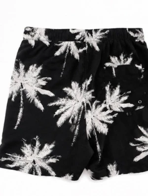 Svarta shorts med palmtryck - Säljer ett par svarta shorts med vita palmträdsmotiv. Shortsen har elastisk midja med snörning och är perfekta för sommaren. Lätta och sköna, passar till strand eller chill dagar.