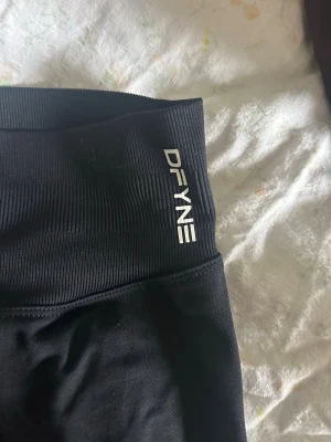 Svarta impact yoga pants från DFYNE - Intressekoll på mina DFYNE impact  i storlek small. De har mellan hög midja och är tillverkade i ett stretchigt material av 90% nylon och 10% elastan. Perfekta för träning eller chill dagar. Snygg logga på linningen. Längd tall. Använt en gång.