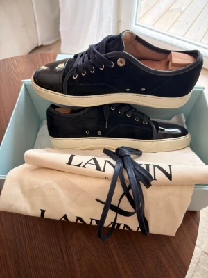 Lanvin skor - Snygga marinblå sneakers från Lanvin med blankt skinn på tå och häl, samt mocka på sidorna. Klassisk design med vita sulor och svarta skosnören. Kommer med original dustbag och box. Perfekt för dig som vill ha en stilren och lyxig look.