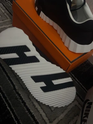Svarta sneakers med vit sula - Snygga svarta sneakers med kraftig, räfflad vit sula och svarta snören. Ovandelen är i textil och mockaimitation, med vita detaljer runt öppningen. Sulan har ett coolt mönster undertill. Perfekta för dig som gillar streetstyle och vill sticka ut.