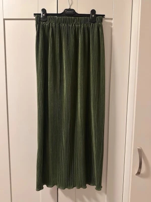 Olivgrön ribbad långkjol - Snygg olivgrön långkjol med ribbad struktur och elastisk midja. Kjolen har en rak passform och är tillverkad i ett mjukt, stretchigt material som ger en bekväm känsla. Perfekt att styla med en enkel topp eller stickad tröja.