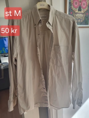 Beige skjorta från Florentino - Klassisk beige skjorta från Florentino med lång ärm och bröstficka. Skjortan har knappar framtill och en stilren, enkel design som passar till många olika outfits.
