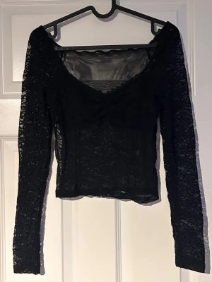 Svart spetstopp - Snygg svart topp i genomskinlig spets med lång ärm och djup v-ringning. Modellen är croppad och är lite tajt så skulle säga att den är en liten S 