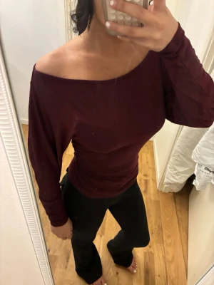 Mörkröd offshoulder topp - Säljer en mörkröd offshoulder topp med lång ärm och tight passform. Toppen har en snygg, enkel design och är tillverkad i ett mjukt, stretchigt material som sitter skönt på kroppen. Perfekt för dig som vill ha en stilren men ändå trendig look.