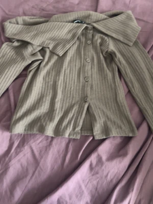 Beige ribbad från Gina Tricot - Säljer en beige ribbstickad cardigan från Gina Tricot med knappar framtill och lång ärm. Tröjan har en bred krage och är gjord i mjukt, stretchigt material. Perfekt att styla med jeans eller kjol. Storlek XS. Använd en fåtal gånger.