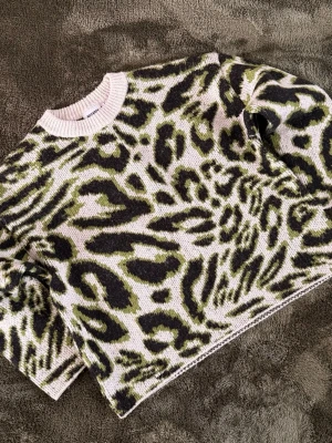 Weekday Stickad tröja med leopardmönster  - Cool stickad tröja från Weekday med leopardmönster i svart och grönt på ljus bakgrund. Tröjan har rund halsringning och ribbstickade muddar. Perfekt för dig som vill sticka ut med din stil.