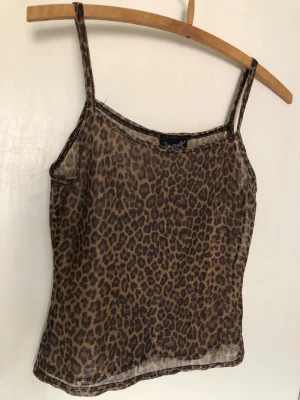 Leopardmönstrad mesh linnetopp - Säljer en leopardmönstrad mesh linnetopp från Von Dutch. Toppen är ärmlös med tunna axelband och har en transparent look som ger en edgy vibe. Perfekt att styla lager på lager eller som statement-piece. Flerfärgad.