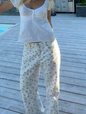 Vita jeans med blommigt mönster från H&M - Säljer ett par vita jeans med små blommiga tryck från H&M. Jeansen har rak passform och hög midja. Klassiska fickor både fram och bak. Perfekta för midsommar🌸Jag är vanligtvis en 36/38 i exempelvis Zara jeans