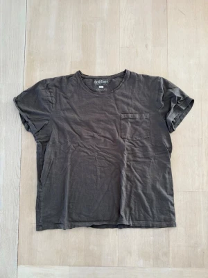 Mörkbrun t-shirt från Dobber - En enkel och stilren t-shirt från Dobber med rund halsringning och en bröstficka. T-shirten har korta ärmar och är tillverkad i mjuk bomull för en skön känsla. Perfekt till jeans eller shorts.