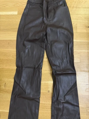 Bruna skinnbyxor med raka ben - Snygga bruna skinnbyxor med raka ben och hög midja. Byxorna har klassisk femficksdesign och stängs med dragkedja och knapp. Perfekta för dig som vill ha en trendig och stilren look med edge.