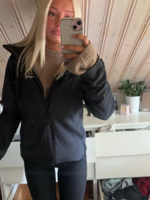 Svart vindjacka från haglöf - Snygg svart vindjacka från Haglöf med dragkedja framtill och hög krage. Jackan har en enkel och stilren design, perfekt för blåsiga dagar. Passar till det mesta och är lätt att matcha med olika outfits. 