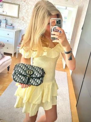 Gul volangklänning med offshoulder - Helt ny, gul kortklänning med volanger och offshoulder-design. Klänningen har smockad överdel och flera lager i kjolen för en luftig känsla. Perfekt för sommarens varma dagar och har en romantisk look. Med prislapp