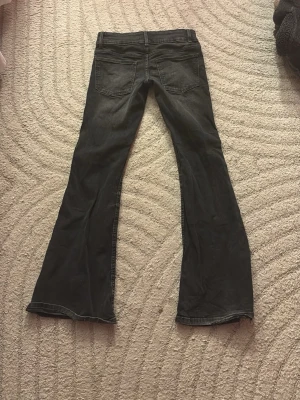 Svarta bootcut jeans med slitningar - Säljer ett par svarta bootcut jeans med slitningar på knäna och råa fållar. Jeansen har fem fickor och två silvriga knappar fram. Perfekta för en avslappnad och trendig look. Pris kan diskuteras💓