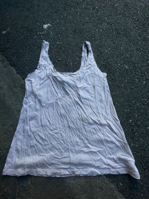 Vit linnetopp från Gina Tricot - Säljer en enkel och luftig vit linnetopp från Gina Tricot. Toppen är ärmlös med breda axelband och har en avslappnad passform. Perfekt att styla till jeans eller shorts för en clean look.