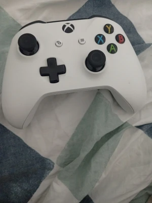 Vit Xbox Series-handkontroll - Säljer en vit Xbox Series-handkontroll med klassisk design och svarta detaljer. Handkontrollen har två analoga spakar, styrkors och färgade knappar (A, B, X, Y). Perfekt för gaming och kompatibel med Xbox Series och PC.
