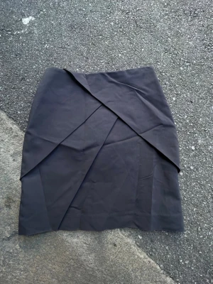 Svart omlottkjol från H&M - Snygg svart omlottkjol från H&M med stilrena lager och dragkedja i sidan. Kjolen har en modern, asymmetrisk design och är perfekt för dig som gillar minimalistisk stil. Tillverkad i ett mjukt polyestertyg som känns bekvämt hela dagen.