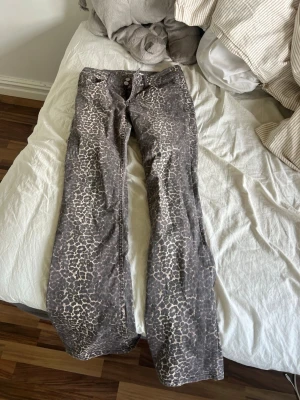 Bootcut leo jeans från Nelly - Säljer ett par bootcut jeans från Nelly med leopardmönster i grå och beige toner. Modellen är low waist och har en snygg utsvängd passform. Perfekta för dig som vill sticka ut med ett djurmönstrat plagg.
