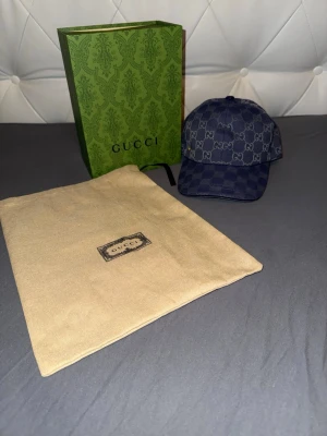 Mörkblå Gucci keps med GG-mönster - Snygg mörkblå keps från Gucci med det klassiska GG-monogrammet över hela kepsen. Kepsen har böjd skärm och justerbar rem bak. Materialet är en blandning av canvas och bomull, vilket ger en exklusiv känsla. Perfekt accessoar för dig som vill sticka ut.