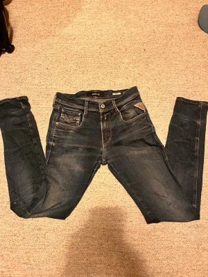 Mörkblå slim fit jeans från Replay - Snygga mörkblå slim fit jeans från Replay med slitningar och kontrastsömmar. Klassisk femficksmodell med läderpatch bak i midjan och detaljerade bakfickor. Perfekta för en trendig och avslappnad stil.