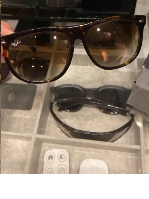 Ray-Ban brunmönstrade solglasögon - Säljer ett par klassiska Ray-Ban solglasögon med brunmönstrad båge och svarta detaljer. Glasen är mörka och bågen har en tidlös, rektangulär form. Medföljer original Ray-Ban fodral. Perfekt för dig som vill ha en ikonisk look.