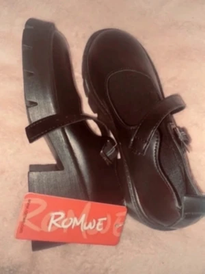 Svarta chunky Mary Jane skor Romwe - Svarta Mary Jane skor med breda remmar och kraftig plattformsula. Skorna har en robust och edgy design med markerade sömmar och grovt mönstrad yttersula. Materialet är syntetiskt och de har en unik look som sticker ut.