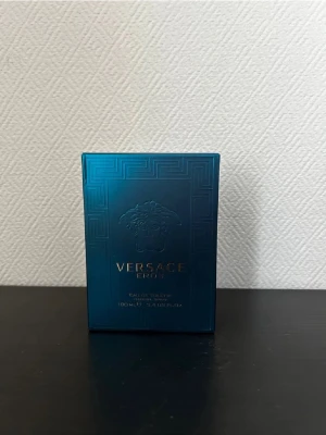 Versace Eros Eau de Toilette 100ml - Versace Eros Eau de Toilette i en snygg blågrön glasflaska med guldiga detaljer och Medusa-logga. Flaskan rymmer 100 ml och har en lyxig, maskulin design. Perfekt för dig som gillar exklusiva och fräscha dofter.