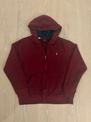 Ralph lauren hoodie - strl 14-16 - Ralph Lauren zip up hoodie 🧥✨ Vinröd färg med gul logga ❤️💛 Storlek 14–16 år, sitter som XS, möjligtvis lite mindre i passformen 👀 Finns ett litet hål på armen, inget stort och inget som syns mycket (kan ses på bild 4)🪡 Snygg och clean hoodie som funkar till många outfits 😎🔥 Hör av er om ni har frågor eller vill ha fler bilder 💬 