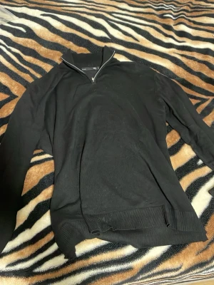 Svart halvzip tröja med krage - Svart långärmad tröja med halvzip och hög krage. Tröjan har ribbade muddar vid ärmslut och nederkant. Perfekt för lager-på-lager och enkel att matcha med jeans eller chinos. Tröjan hade ett litet hål men sydde överser så det syns knappt som du kan de på tredje bilden.