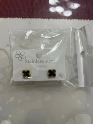 Svarta fyrklöverörhängen i stål - Snygga örhängen i form av små svarta fyrklöver med guldfärgad kant. Tillverkade i rostfritt stål och perfekta för dig som gillar stilrena accessoarer med en twist. Kommer i förpackning.