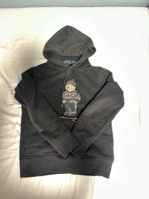 Ralph lauren svart hoodie - Säljer nu denna riktigt fräscha svarta Ralph lauren hoodie med Ralph Lauren björn motiv på framsidan, hoodien är i gott skick och storlek XS🙌tveka inte på att fråga frågor till mig om hoodien!🌟🍾😁