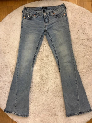 Ljusblå bootcut jeans från True Religion - Snygga ljusblå bootcut jeans från True Religion med klassiska kontrastsömmar och fem fickor. Jeansen har en lätt tvättad look och ikoniska bakfickor med lock och knapp. Perfekta för dig som gillar en avslappnad men trendig stil. Nyskick, endast använda en gång, säljer pågrund av att storleken inte passade mig! Nypris 1399 kr säljer för 1000 kr, priset kan diskuteras vid snabb affär!💕Perfekta jeans till våren!😚