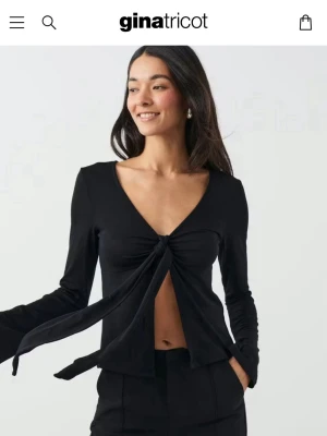 Svart långärmad knytblus Gina Tricot - Trendig svart långärmad topp från Gina Tricot med v-ringning och knyt framtill. Modellen är croppad och har en öppen front som ger en cool look. Perfekt att matcha med höga byxor för en snygg outfit.