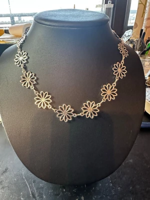 Silverfärgat halsband med blommor - Säljer ett snyggt halsband i silverfärg med flera stora blommor som länkas ihop. Blommorna har en öppen design och ger ett coolt och lekfullt intryck. Perfekt accessoar för att lyfta din outfit med en unik touch. Materialet är metall. Detta är ca 44 cm långt 