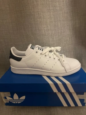 Adidas Stan Smith vita sneakers - Klassiska vita Adidas Stan Smith sneakers med mörkblå detalj på hälen. Helt nya skor, utan användning. Köpta från JD💗