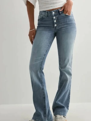 Ljusblå utsvängda jeans med knappar - Snygga ljusblå jeans med utsvängda. Jeansen har fyra synliga guldknappar framtill och klassiska fickor både fram och bak. 