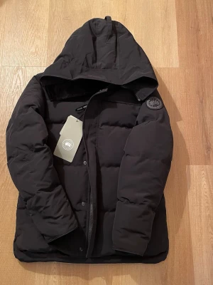 Svart pufferjacka från Canada Goose - Säljer en svart pufferjacka från Canada Goose i storlek M. Jackan har huva, diskret logga på ärmen och dragkedja framtill. Perfekt för kalla dagar och riktigt skön att bära. Klassisk, stilren design som funkar till allt.