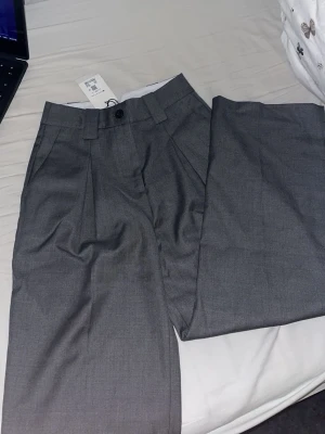 Grå kostymbyxor från Bik Bok - Snygga grå kostymbyxor från Bik Bok i ullblandning. Byxorna har pressveck, hällor för bälte och stängs med knapp och dragkedja. Perfekta för en clean och stilren look.