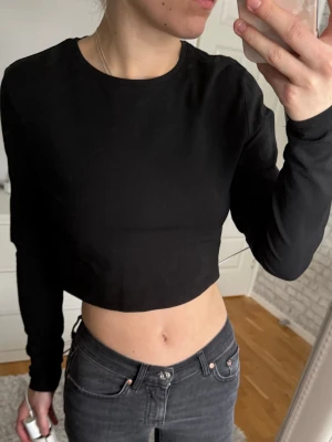 Svart croppad långärmad topp 157 - Svart croppad långärmad topp från 157. Enkel och stilren design med rund halsringning. Tillverkad i mjuk bomull med lite stretch för en skön passform. Perfekt att matcha med jeans eller kjol.