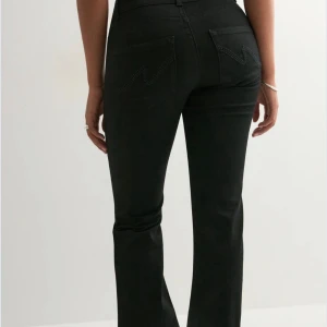 Svarta bootcut jeans med hög midja - Snygga svarta bootcut jeans med hög midja och klassiska fem fickor. Jeansen har utsvängda ben och dekorativa sömmar på bakfickorna. Tillverkade i ett stretchigt denimtyg som sitter bekvämt och formar sig efter kroppen.