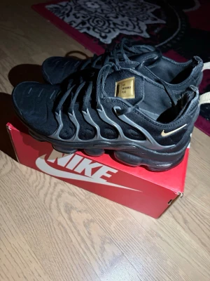 Svarta VaporMax - Säljer ett par svarta Nike sneakers i mycket bra skick. Stilren design med grå detaljer och en guld Nike-logga. Bekväm sula med bra dämpning. Sparsamt använda och original skokartong ingår.