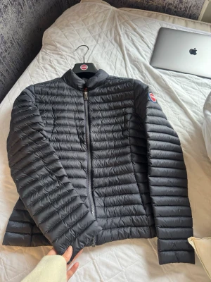 Svart dunjacka från Colmar - Snygg svart dunjacka från Colmar med quiltad design och diskret logga på ärmen. Jackan har dragkedja framtill, ståkrage och smal passform. Perfekt för kalla dagar och enkel att matcha med olika outfits.