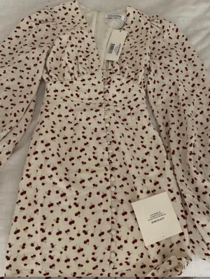 Adoore kort klänning cherry - Supersöt vit kortklänning från Adoore med rött körsbärsmönster! Endast använd en gång. Nypris 1500❤️