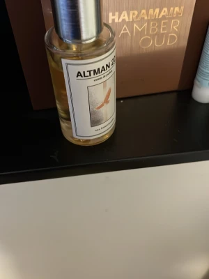 Altman 22.0 Extrait de Parfum - En stilren parfymflaska från Altman med silverfärgad kork och transparent glas. Etiketten har en minimalistisk design med en fågel och texten 'Altman 22.0 Extrait de Parfum'. Doften är exklusiv och flaskan känns lyxig och modern.