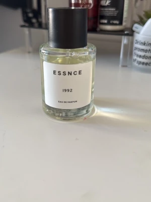 ESSNCE 1992 Eau de Parfum - Minimalistisk parfymflaska från ESSNCE med doften 1992. Flaskan är genomskinlig med svart lock och vit etikett. Modern och stilren design som passar perfekt på parfymhyllan.