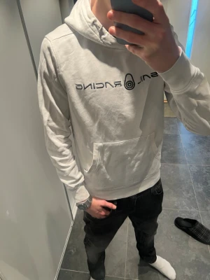Sail racing hoodie  - Säljer en vit hoodie från SNL Racing med svart tryck på bröstet. Hoodien har en klassisk huva med dragsko och en stor magficka framtill. Tillverkad i mjukt material som känns skönt mot huden. Perfekt för dig som gillar streetwear och enkel stil.