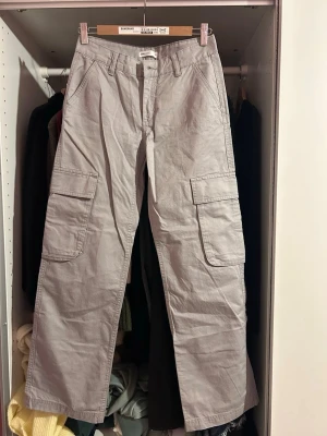 Grå cargobyxor från Perfect Jeans - Säljer ett par grå cargobyxor från Perfect Jeans med raka ben och stora sidofickor med lock. Byxorna har klassisk cargodesign och är tillverkade i ett slitstarkt bomullsmaterial. Perfekt för dig som gillar en avslappnad och trendig stil.