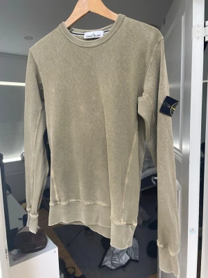 Olivgrön sweatshirt från Stone Island - Säljer en olivgrön sweatshirt från Stone Island med klassisk rund hals och ribbade muddar. Tröjan har den ikoniska logotypen på vänster ärm och är tillverkad i mjukt bomullsmaterial. Perfekt för en avslappnad och stilren look.Köpt för 1300 från soleplus och authentic testad