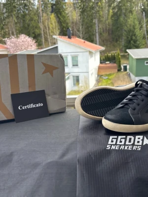 Svarta GGDB Superstar sneakers - Snygga svarta GGDB Superstar sneakers med svart stjärndetalj på sidan och vit sula. Skorna har glitter på hälen och klassiska svarta skosnören. Tillverkade i läder och kommer med originalpåse och certifikat.